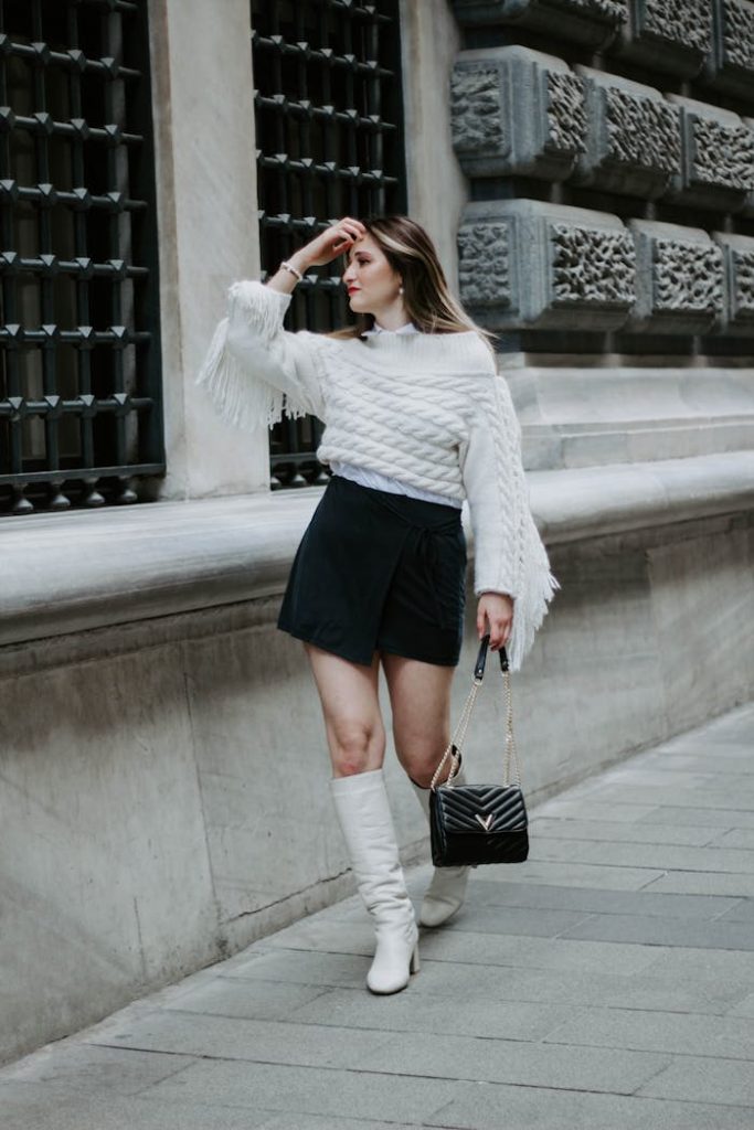Fashionable woman in white sweater and boots strolling a historic street in Istanbul.