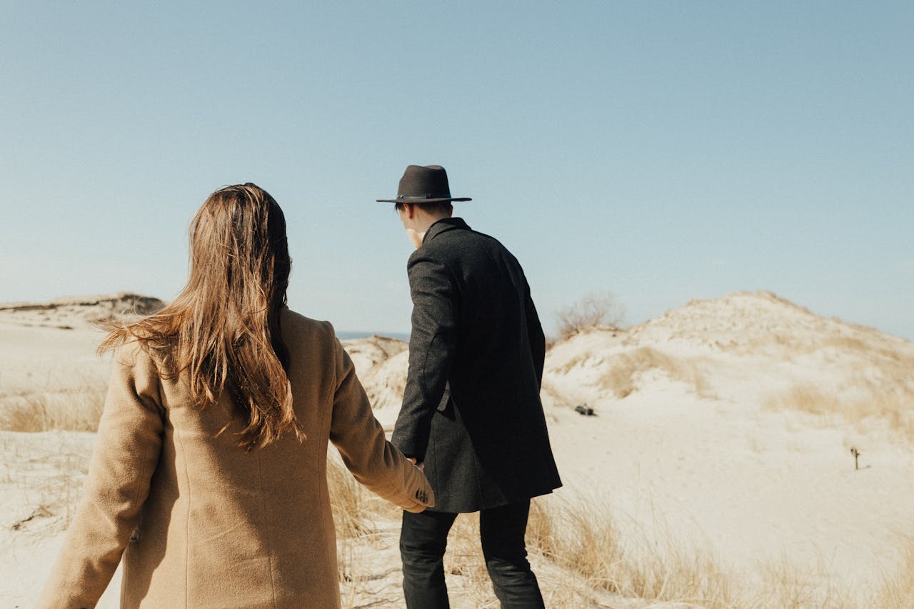 A couple walks hand in hand through a serene desert. Captivating back view under the clear sky.