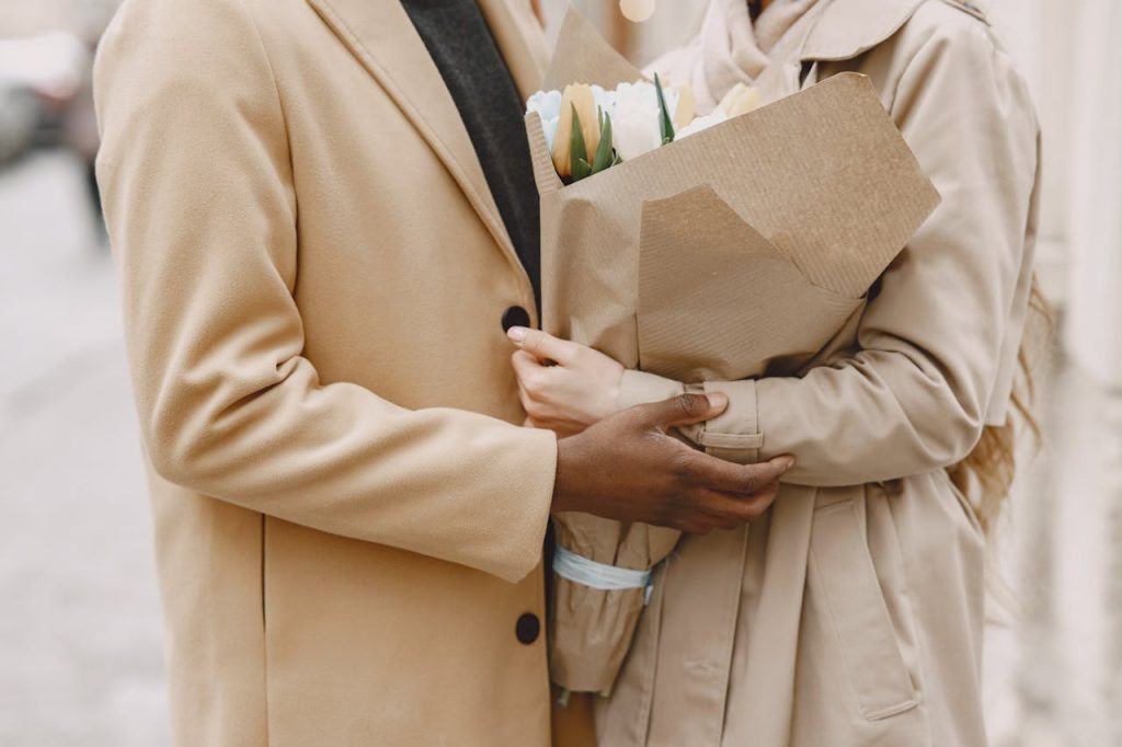 Close-up of a couple in coats holding a tulip bouquet, embracing outdoors.