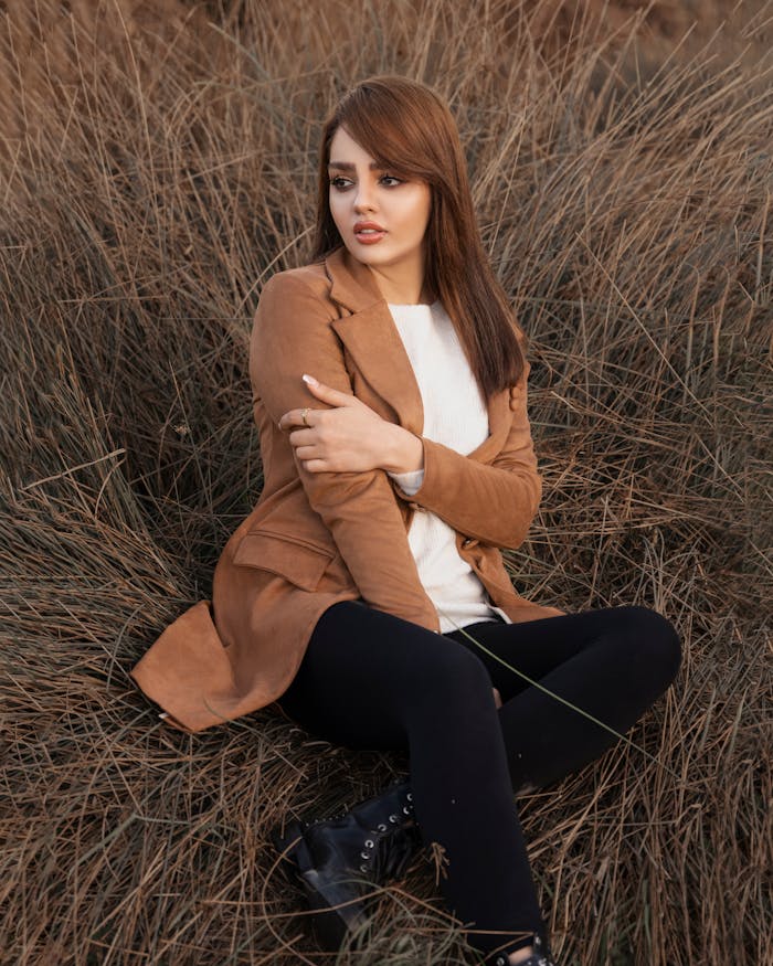 Portrait of a woman with long hair sitting in dried grass looking away.